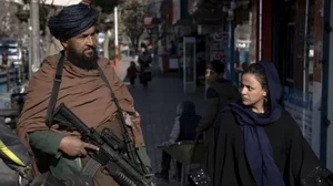 A Taliban fighter stands guard as a woman walks past in Kabul, Afghanistan, on December 26, 2022. 