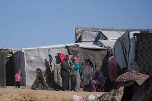 AP Photo/Abdel Kareem Hana : Palestinian families sit outside of tents made locally from pieces of cloth and nylon, in a camp for internally displaced Palestinians at the beachfront in Deir al-Balah, central Gaza Strip, Friday, Dec. 27, 2024.