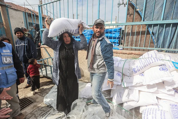 Palestinians carry the flour they received from UNRWA.