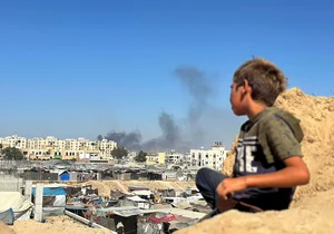 (Photo by Doaa Albaz/Anadolu via Getty Images) : A Palestinian child hides near the rocks as smoke rises from the Hamed area following an Israeli attack