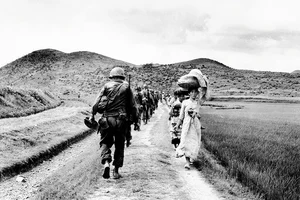 | Photo: Getty Images : Two Faces of a War: A line of US Army soldiers file past a group of Korean women and children during the 1950-1953 Korean War