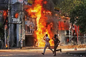 | Photo: AP : Waves of Unrest: People run past a shopping centre, which was set on fire in Dhaka, Bangladesh, in August 2024